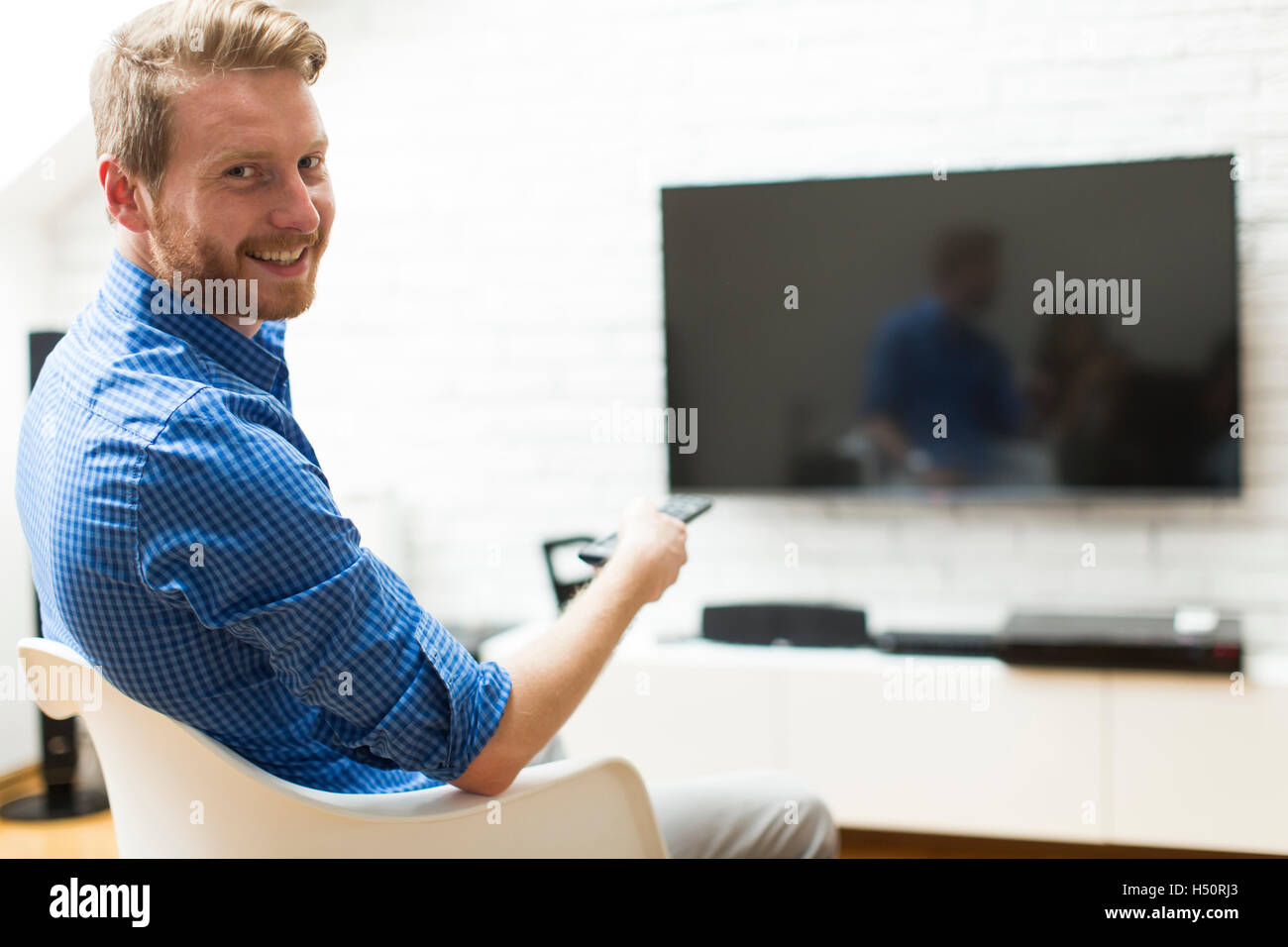 Man with a tv remote control sitting in a living room Stock Photo