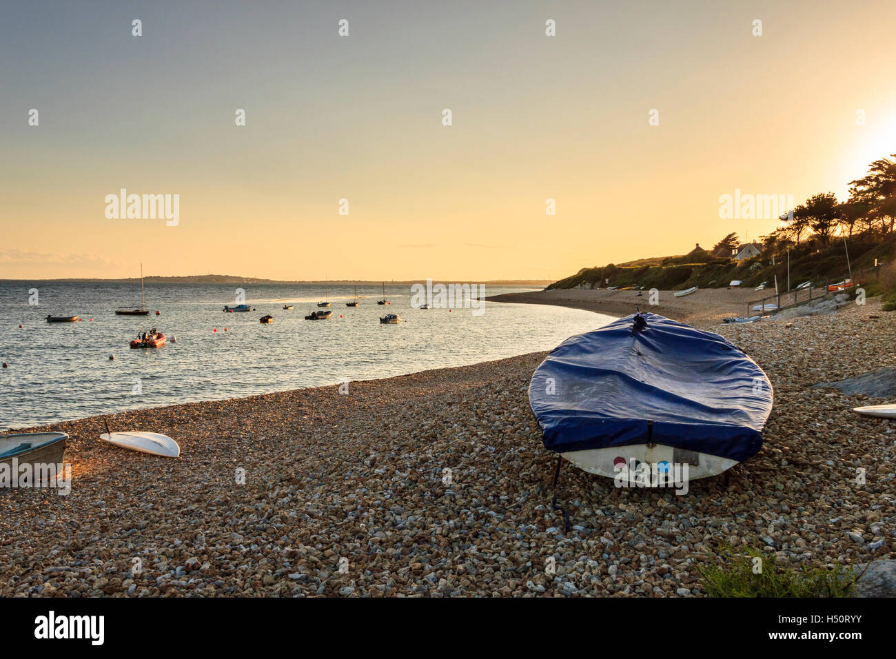 Sunset at Ringstead Bay, Dorset, UK, sailing boats moored in the bay and a tarpaulin-covered dinghy on the shingle beach in the foreground Stock Photo