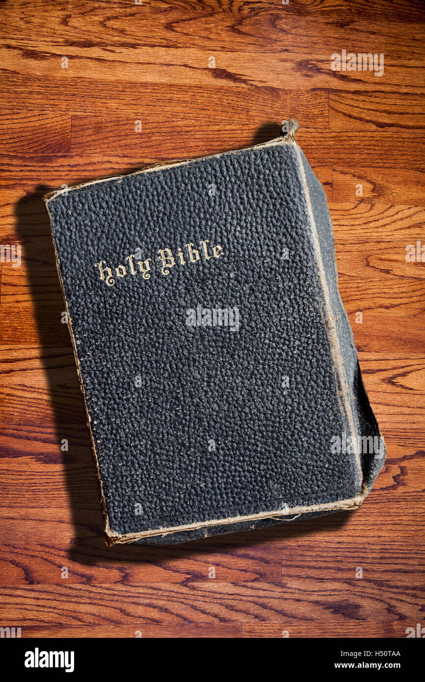 An old Bible against a wood textured background and copy space. Deliberate side lighting with hard shadow for dramatic effect. Stock Photo
