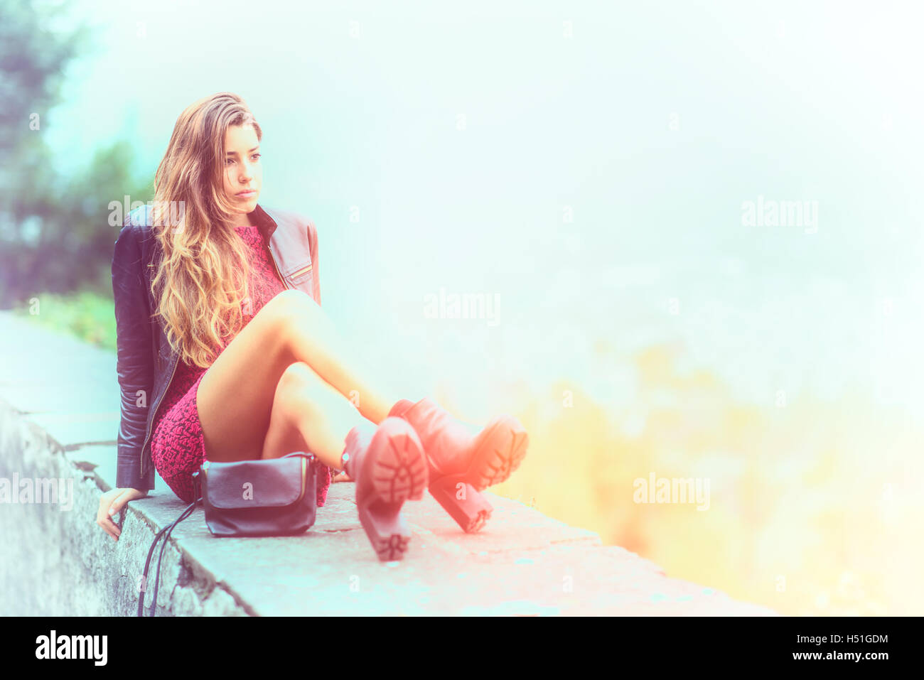 Teen girl with long hair sitting on a low wall Stock Photo - Alamy