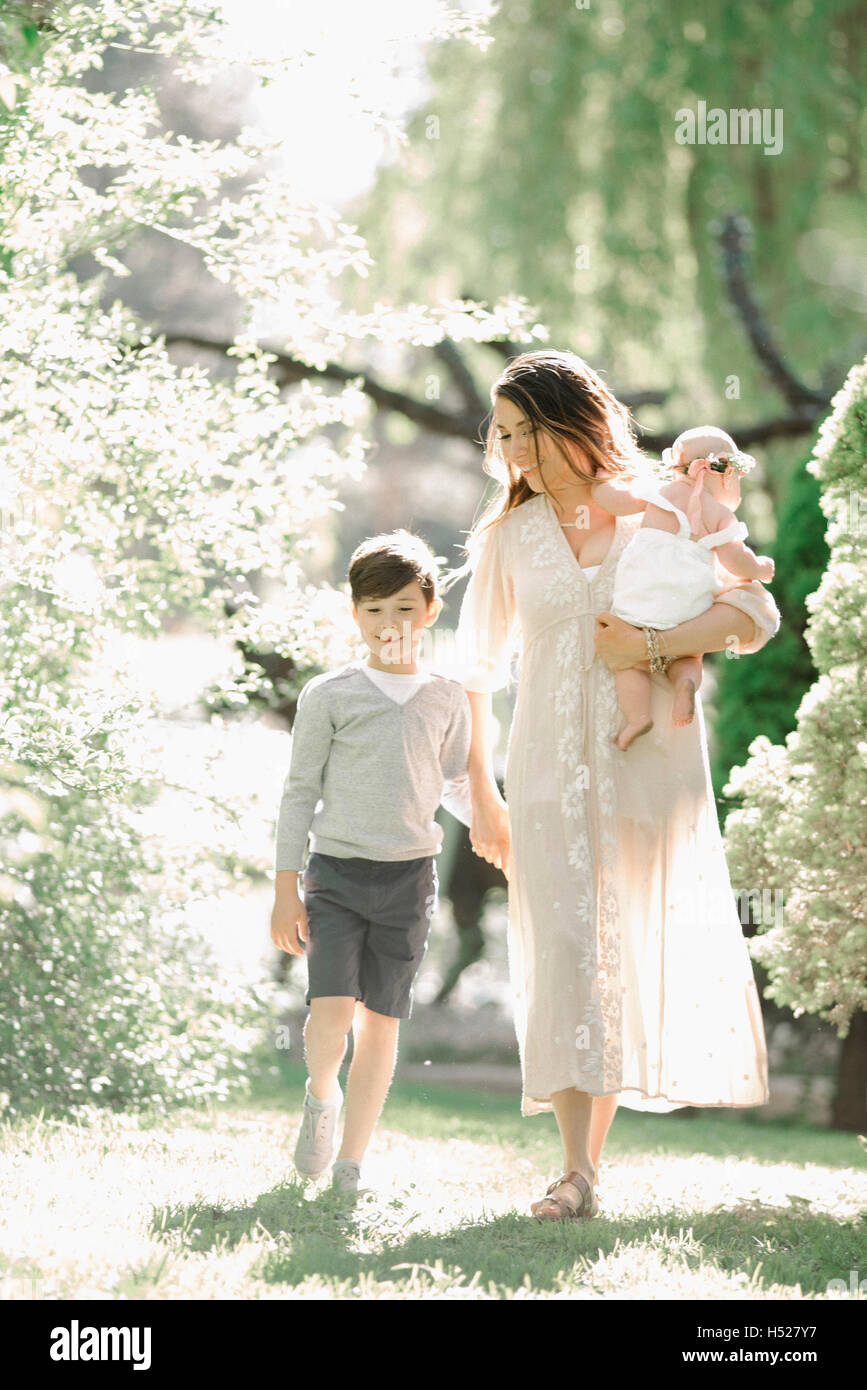 Portrait of a smiling mother, boy and baby girl with a flower wreath on her head, walking in a garden. Stock Photo