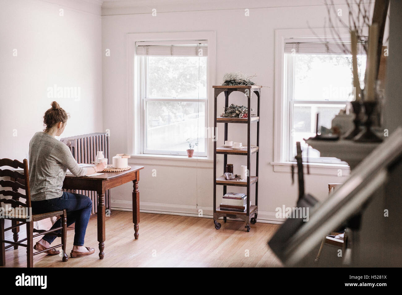 Woman sitting at a table in her apartment, writing in a diary, morning routine. Stock Photo