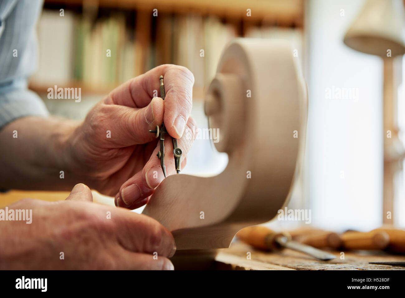 A violin maker working in his workshop, using hand tools to shape and chisel the curled scroll of the violin stock. Stock Photo