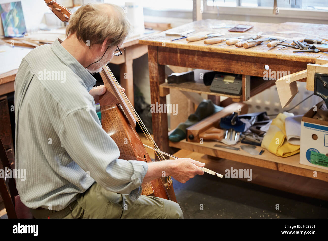 A violin maker in his workshop playing instrument with a bow, tuning and finishing. Stock Photo