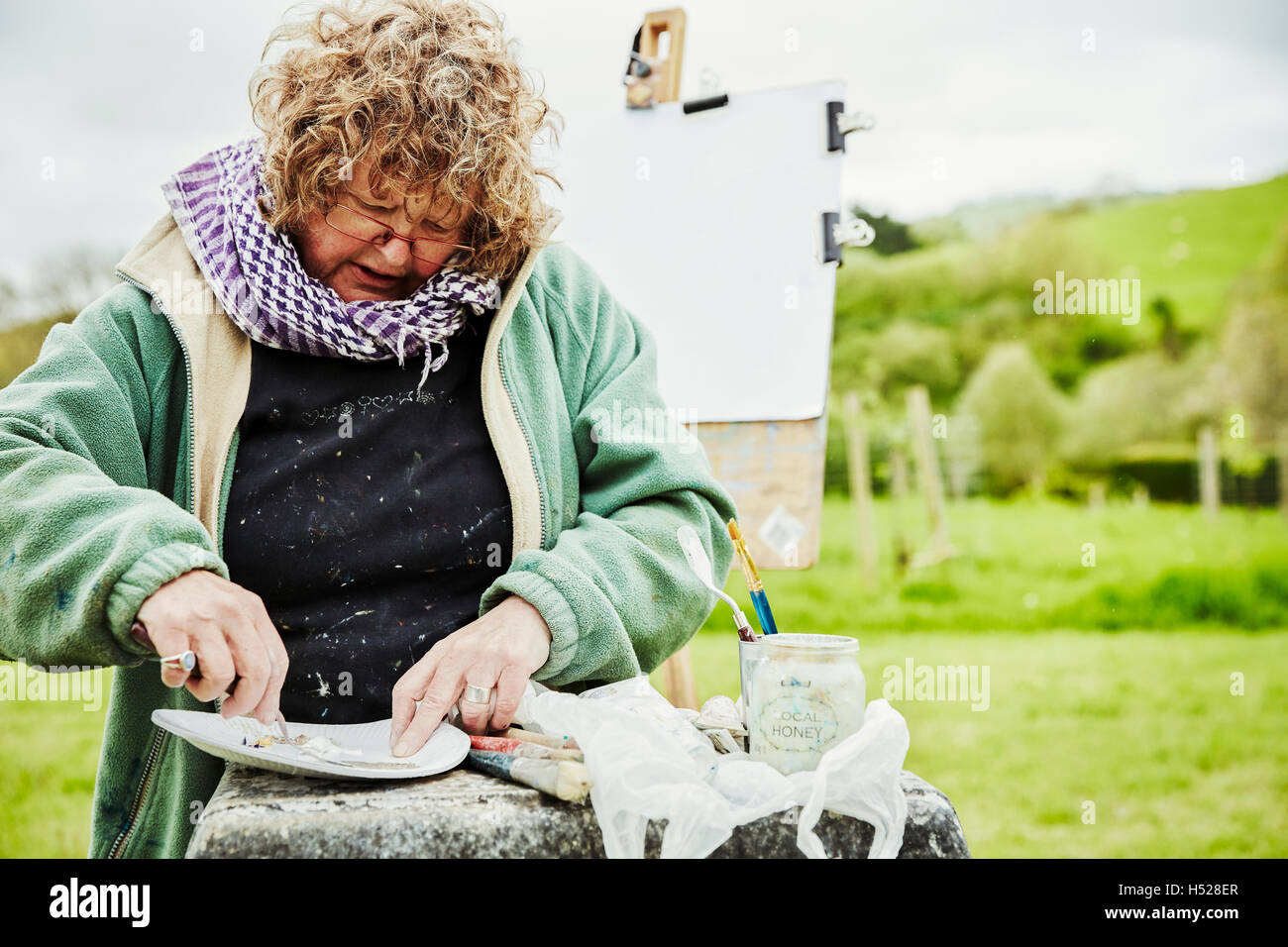 A woman artist working outdoors, sitting mixing or preparing paint on a paper plate. Stock Photo
