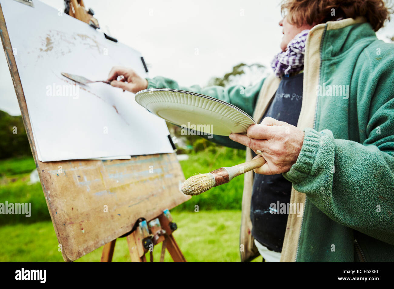 A woman artist working at her easel outdoors, applying paint with a hand tool. Stock Photo