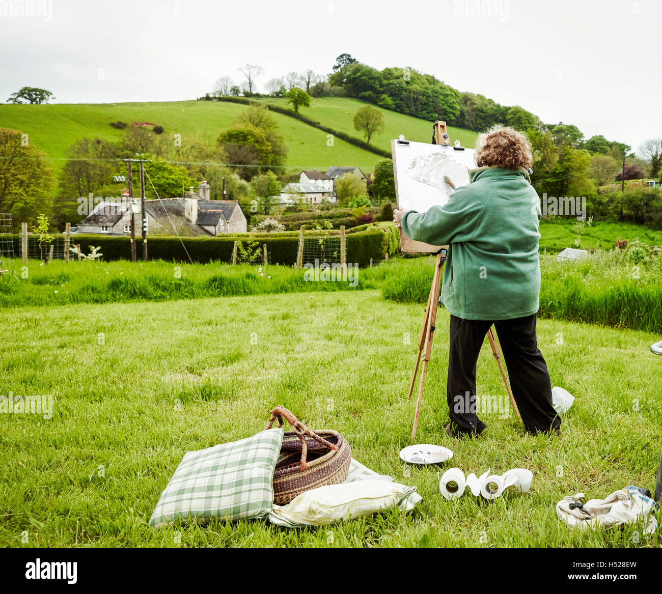 A woman artist outdoors at easel, painting a rural scene. Stock Photo