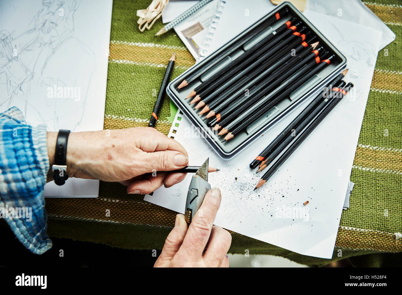 A person using a sharp blade, a craft knife, to sharpen lead pencils. Sketches on paper. Stock Photo