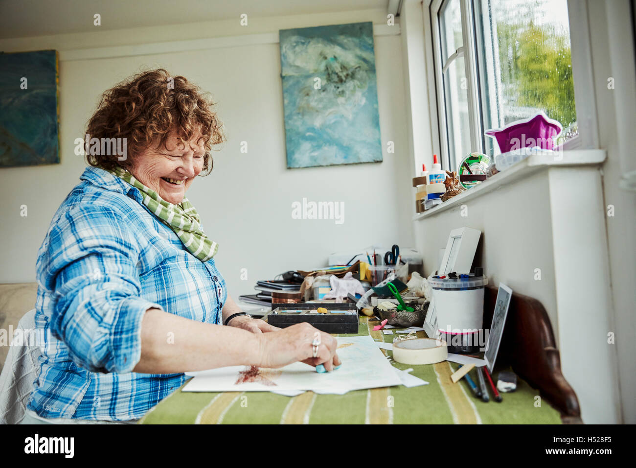 A woman artist working at a table, using a large blue pastel crayon and drawing on paper. Stock Photo