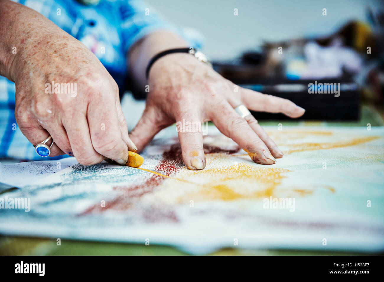 An artist working, hands drawing on the surface of a canvas with a yellow pastel colour. Stock Photo
