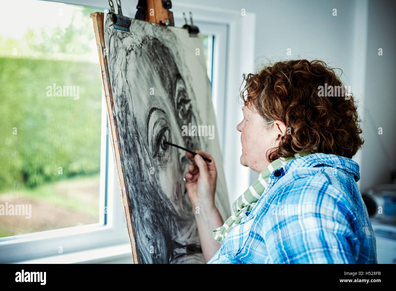An artist working at her easel, using charcoal on paper drawing a portrait. Stock Photo
