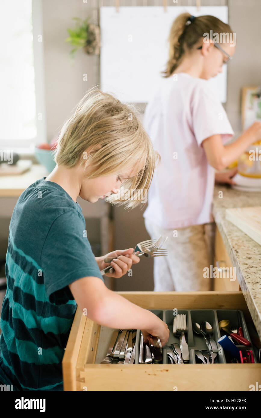 Family preparing breakfast in a kitchen, boy getting cutlery from a drawer. Stock Photo