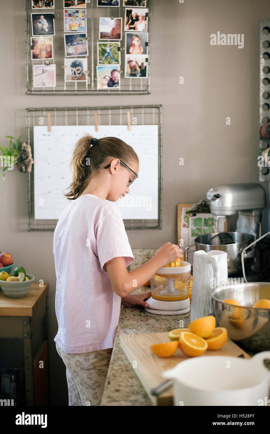 Family preparing breakfast in a kitchen, girl squeezing oranges. Stock Photo