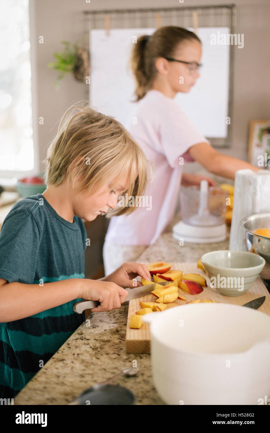 Family preparing breakfast in a kitchen, boy cutting fruit. Stock Photo