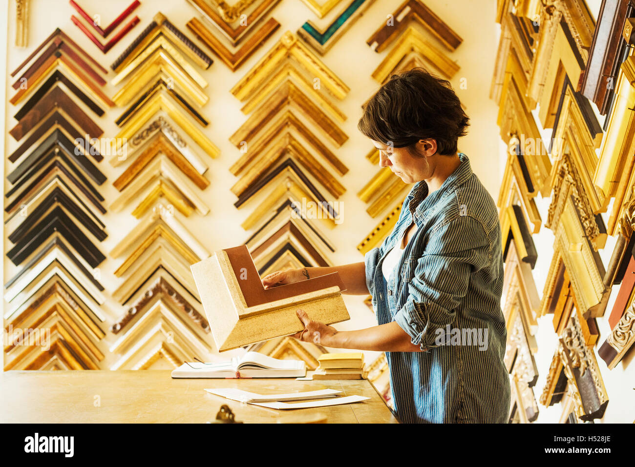 Woman working at a picture framers, a large selection of frames on the
