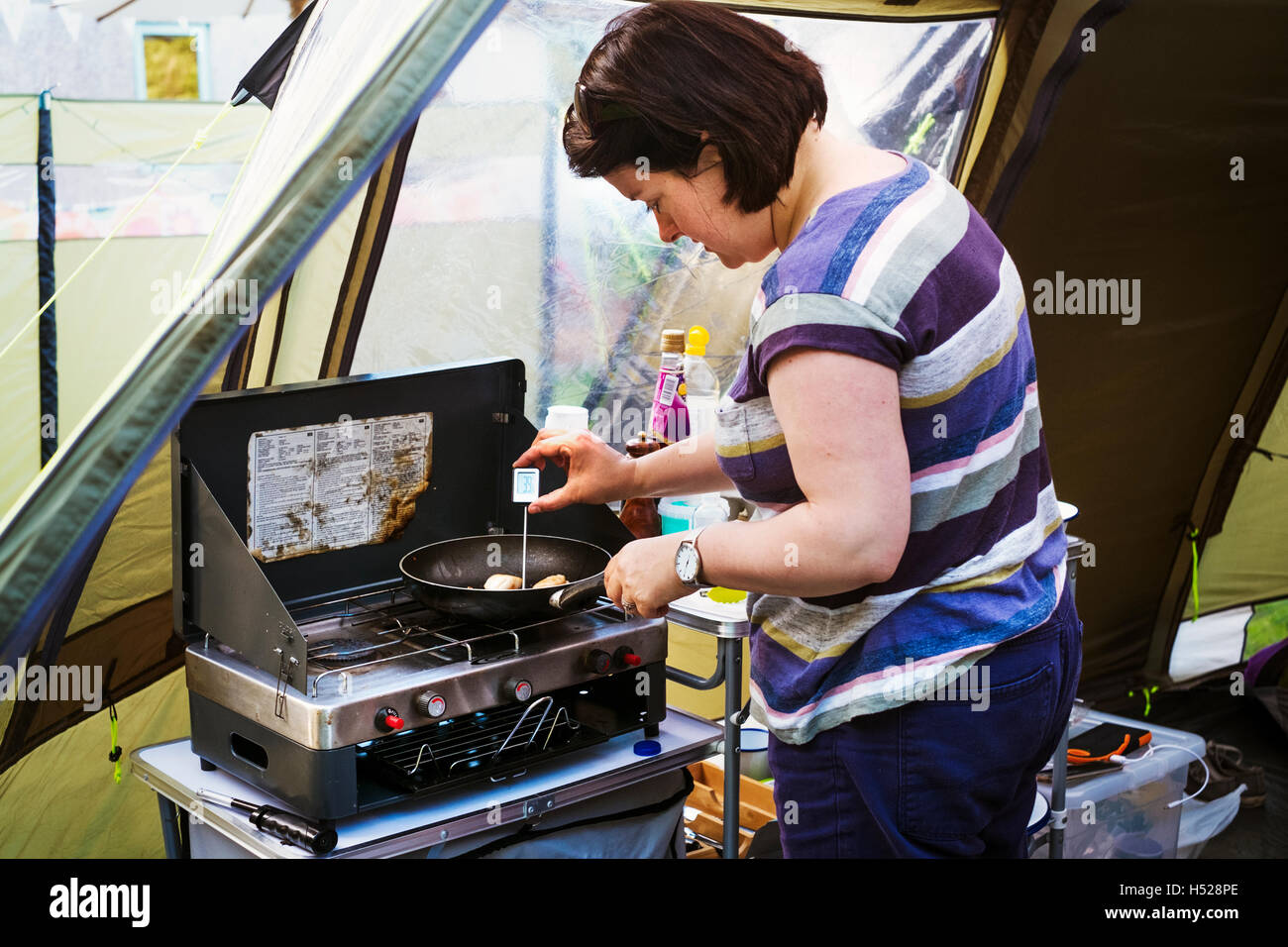 Woman at a camping stove, measuring the temperature of a scallop in a frying pan with a digital thermometer. Stock Photo