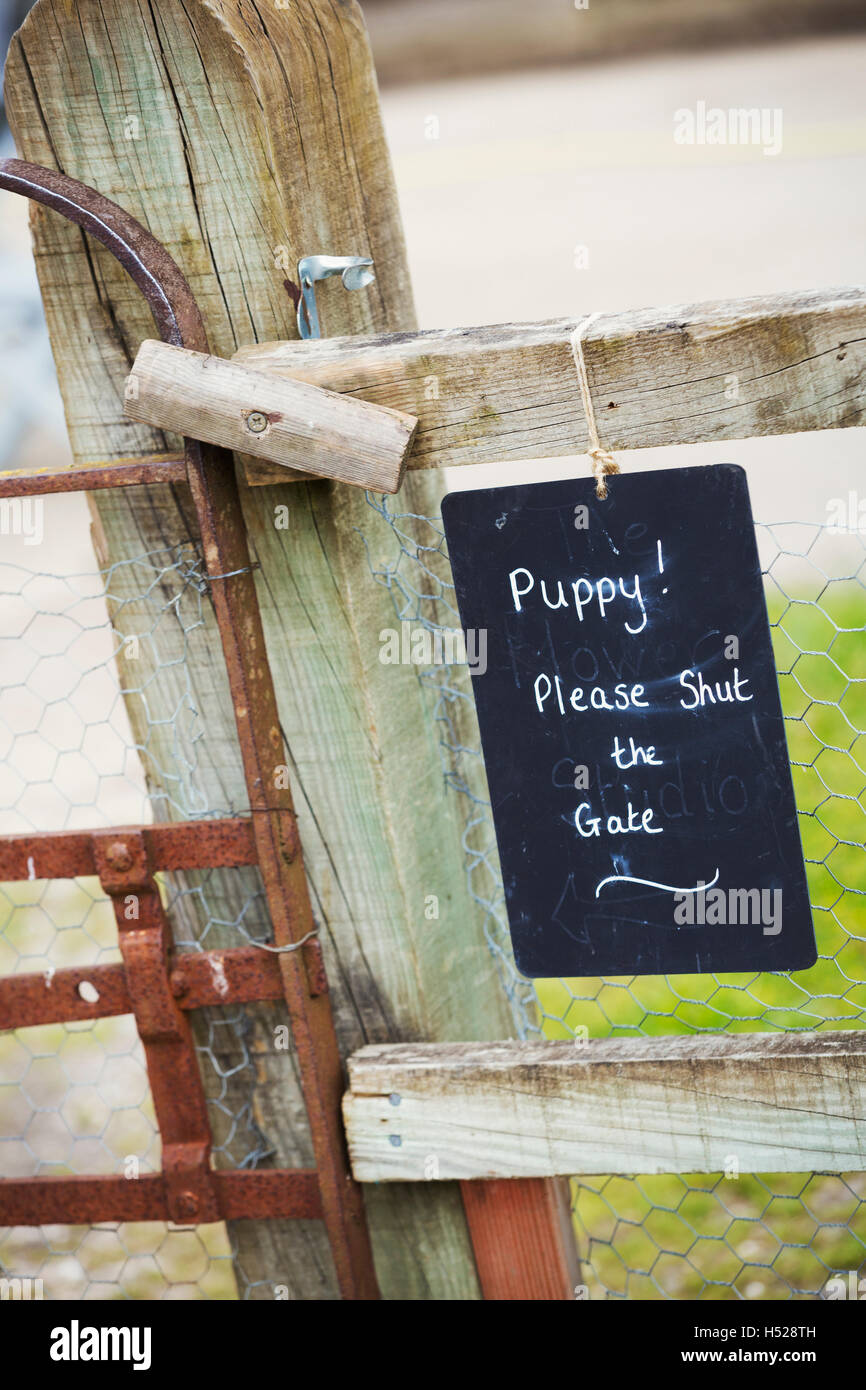 A chalk sign on a garden gate Puppy! Please shut the gate. Stock Photo