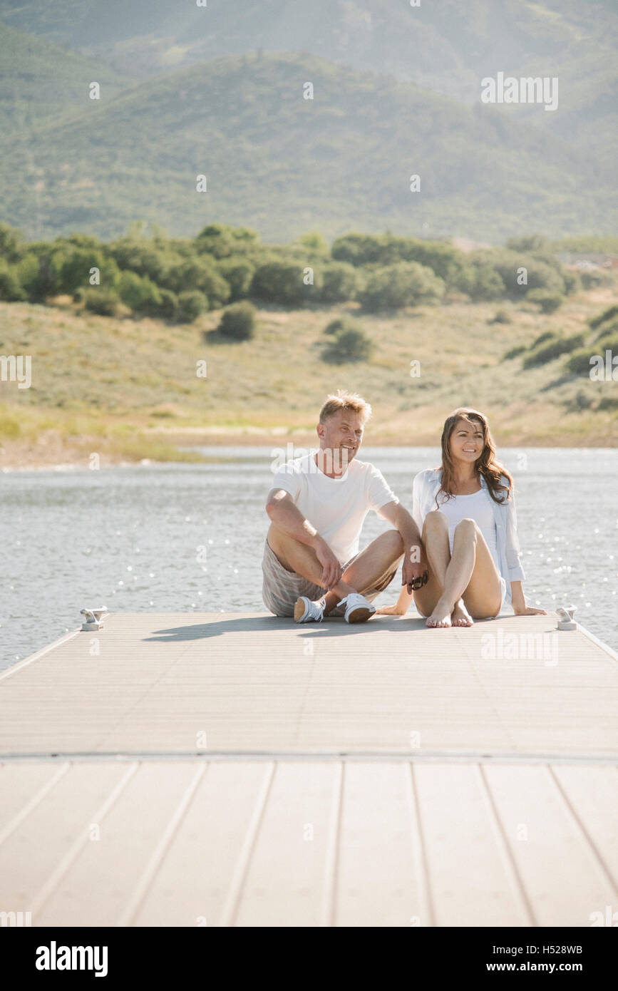 Man and woman sitting side by side on a jetty. Stock Photo