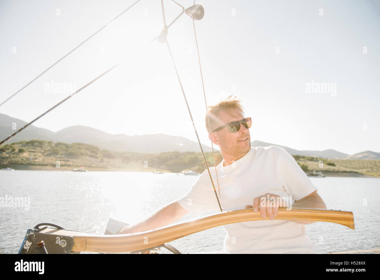 Portrait of a blond man with sunglasses steering a sail boat. Stock Photo
