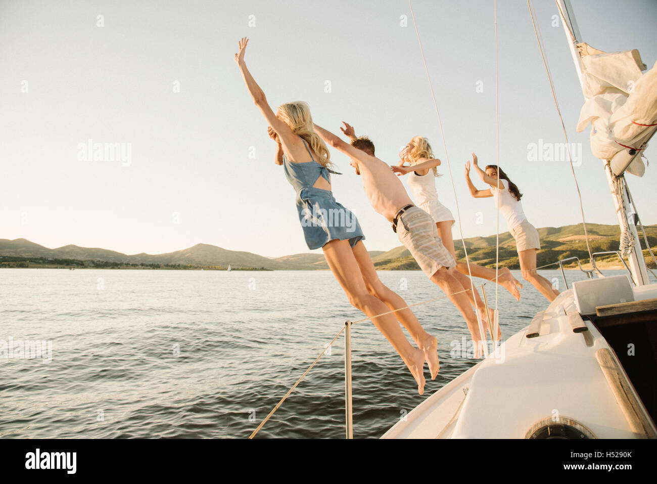 Four people jumping off the side of a sail boat into a lake Stock Photo