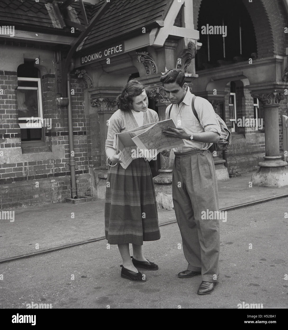 1950s, historical, a young adult couple dressed in normal everyday clothing, study a map outside a train station, before embarking on a day's walking or rambling, England. Stock Photo