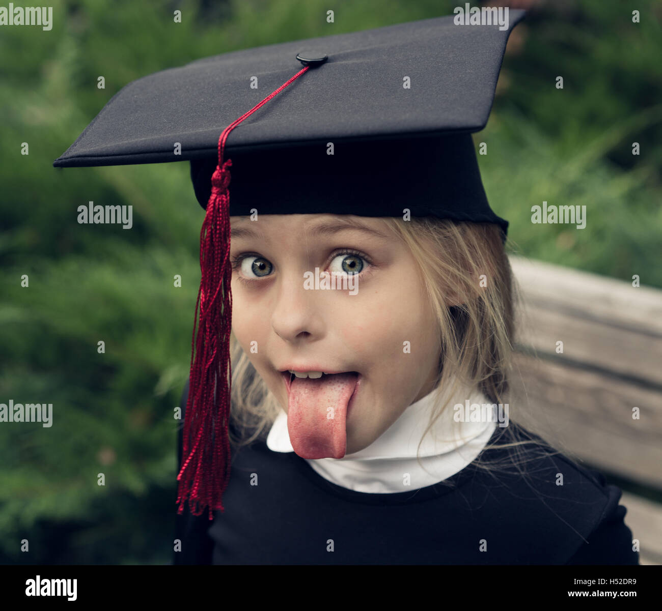 Beautiful blond girl in school uniform and graduation cap on his head sticks out tongue as Albert Einstein. Stock Photo