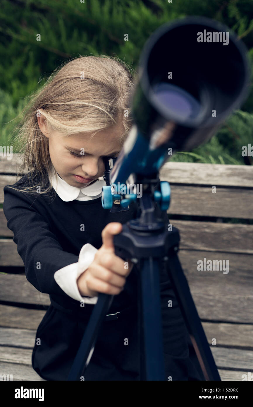 Beautiful blond girl in a school uniform in the park looking through  telescope Stock Photo