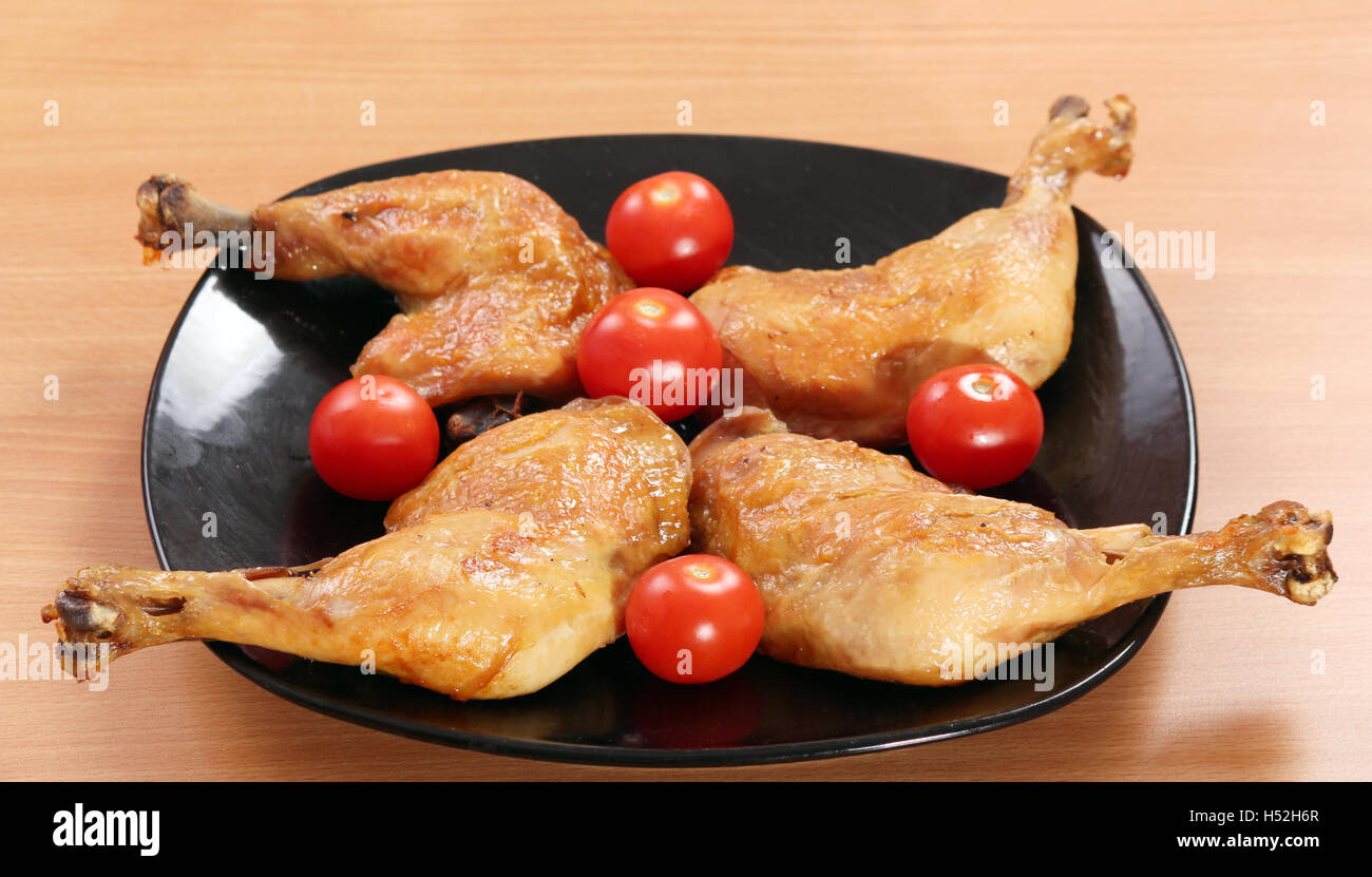 chicken drumstick and tomatoes on black dish Stock Photo