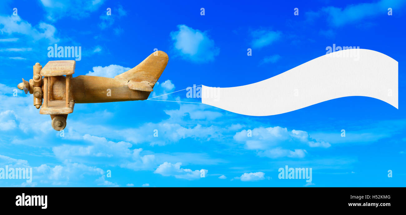 Vintage wooden toy plane flying in blue sky pulling a blank white banner ready for your message Stock Photo