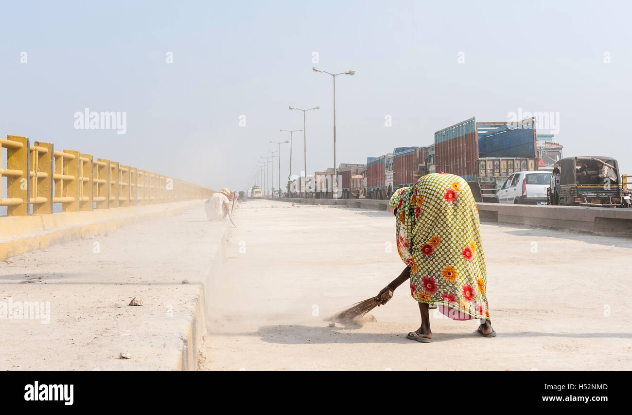 Woman sweeps one lane of the Mahatma Gandhi bridge during refurbishment while there is a long traffic jam in other lane. Stock Photo