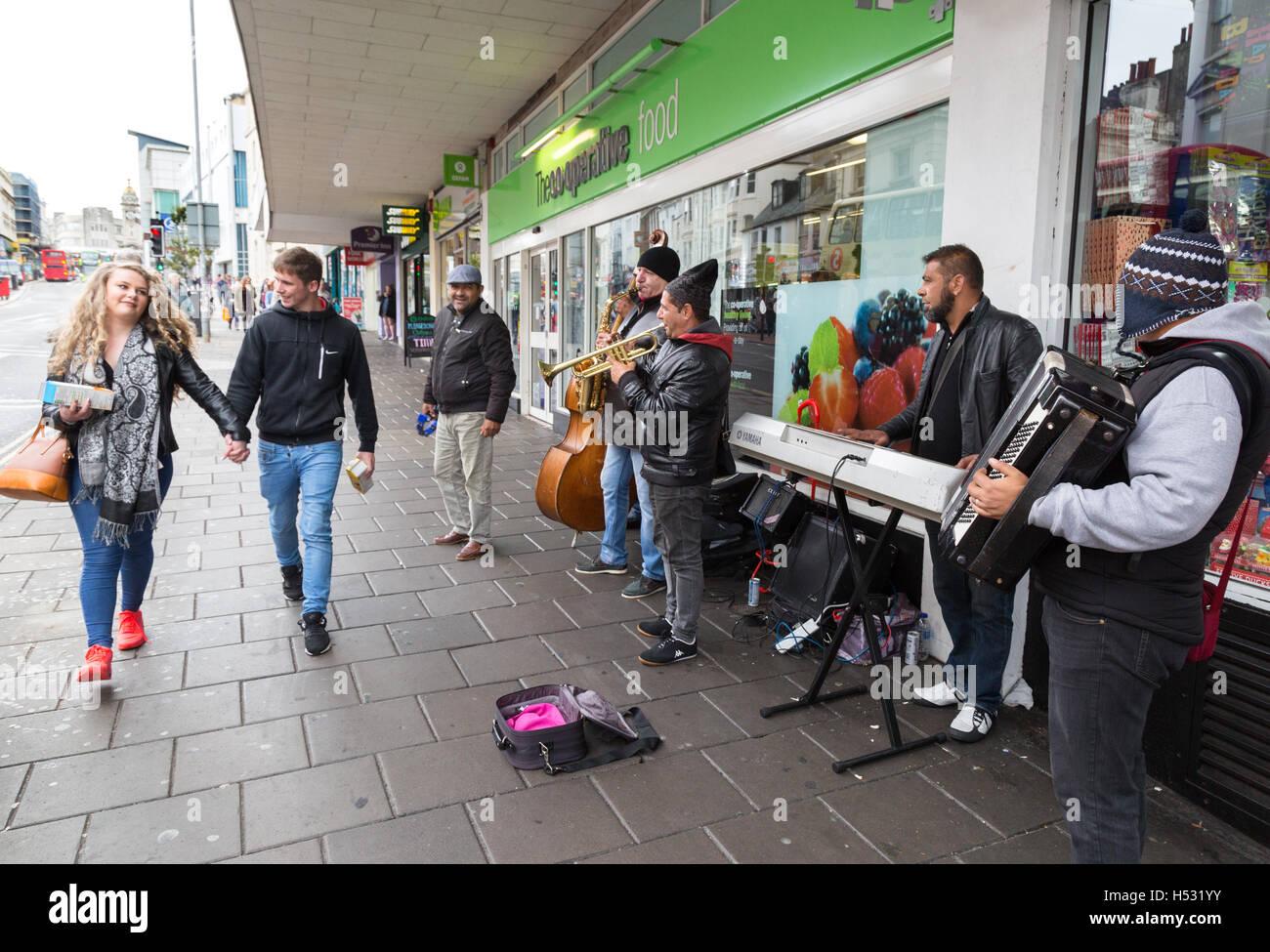 A couple walking past a band busking, the Lanes, Brighton, Sussex UK Stock Photo