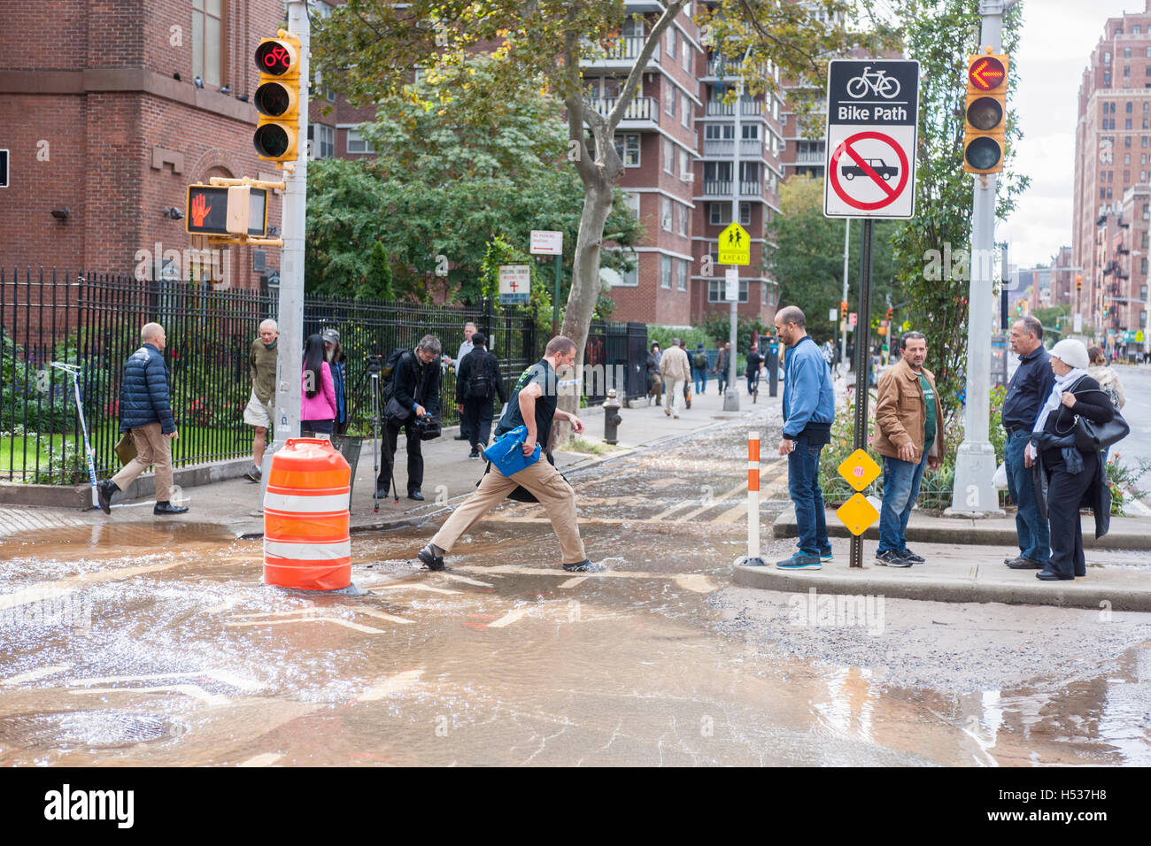 Pedestrians maneuver through flowing water from a watermain break  in the Chelsea neighborhood of New York on Wednesday, October 12, 2016. The watermain break caused water to gush but it was mostly contained to the street safely running into storm drains. (© Richard B. Levine) Stock Photo