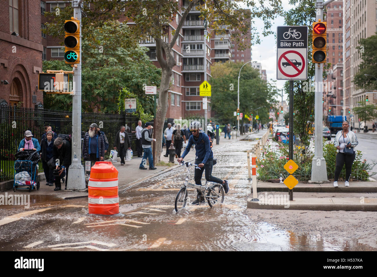 Bicyclists maneuver through flowing water from a watermain break  in the Chelsea neighborhood of New York on Wednesday, October 12, 2016. The watermain break caused water to gush but it was mostly contained to the street safely running into storm drains. (© Richard B. Levine) Stock Photo