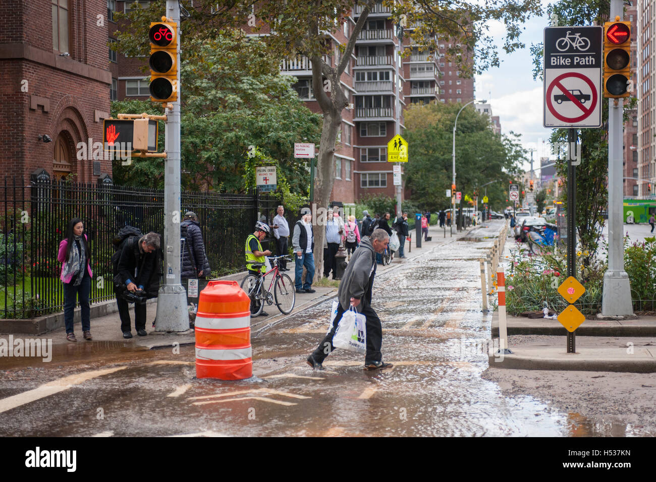 Pedestrians maneuver through flowing water from a watermain break  in the Chelsea neighborhood of New York on Wednesday, October 12, 2016. The watermain break caused water to gush but it was mostly contained to the street safely running into storm drains. (© Richard B. Levine) Stock Photo