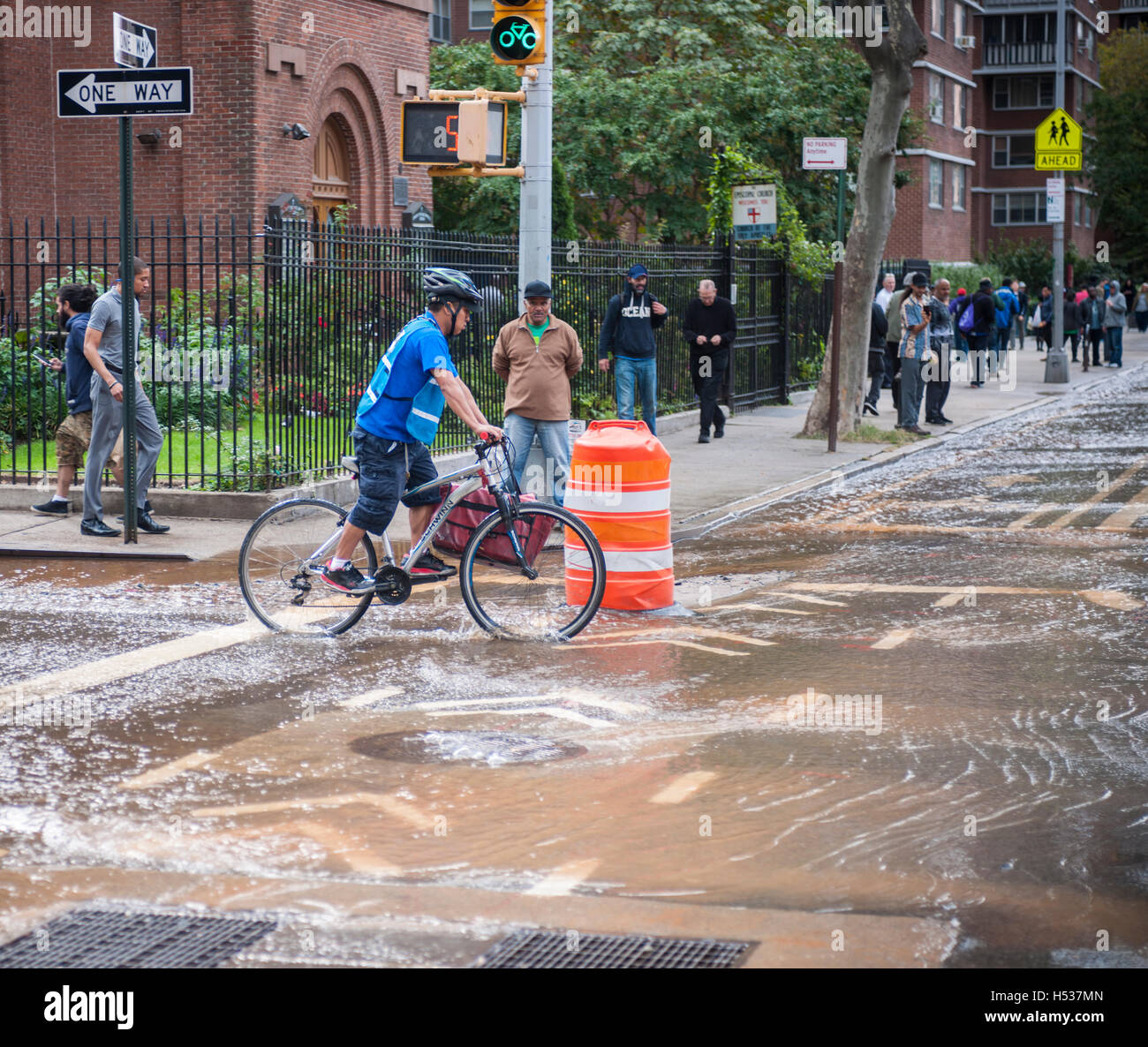 Bicyclists maneuver through flowing water from a watermain break  in the Chelsea neighborhood of New York on Wednesday, October 12, 2016. The watermain break caused water to gush but it was mostly contained to the street safely running into storm drains. (© Richard B. Levine) Stock Photo