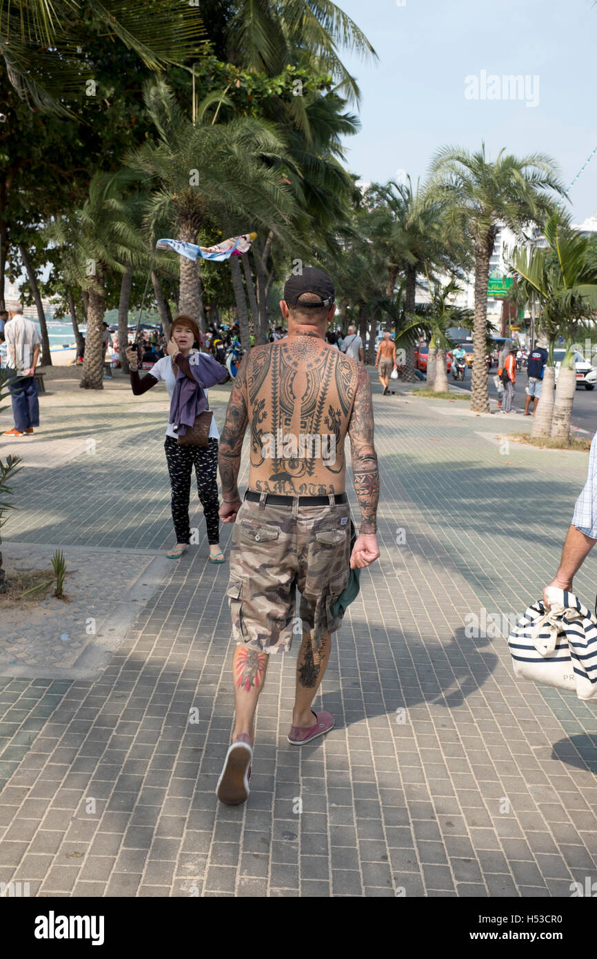 Tattooed Man walking along beach front in Pattaya Thailand Stock Photo