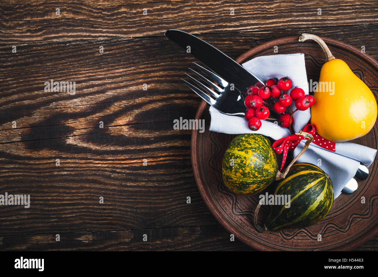 Rustic autumn place setting, ceramic plate, knife and fork wrapped with napkin on rustic wooden table, top view, Thanksgiving Stock Photo