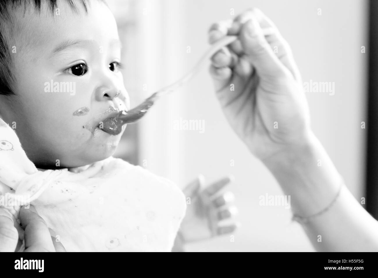 baby looking while feeding Eating Healthy Porridge Food, soft black and white color low key style. Stock Photo