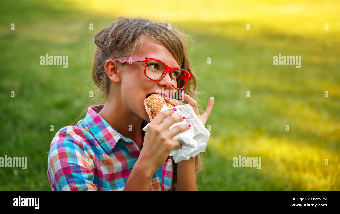 Pretty attractive girl eating a hot dog in a park. Snack. Fast food. Stock Photo