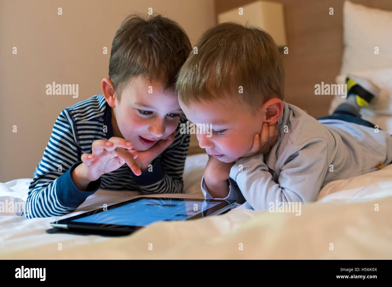 Two boys, siblings lying on a bed and playing with an iPad, Tablet PC Stock Photo