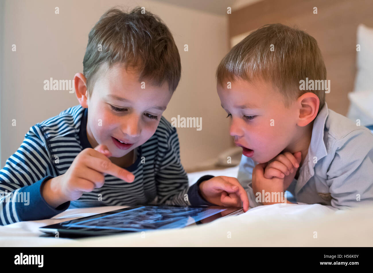 Two boys, siblings lying on a bed and playing with an iPad, Tablet PC Stock Photo