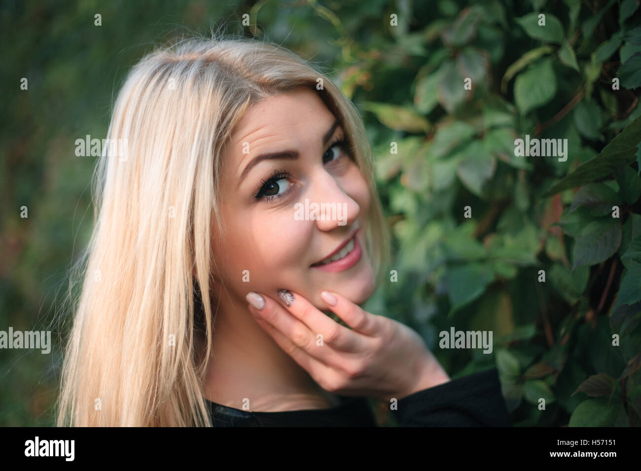 Portrait of an attractive young woman on a background of green ivy leaves Stock Photo