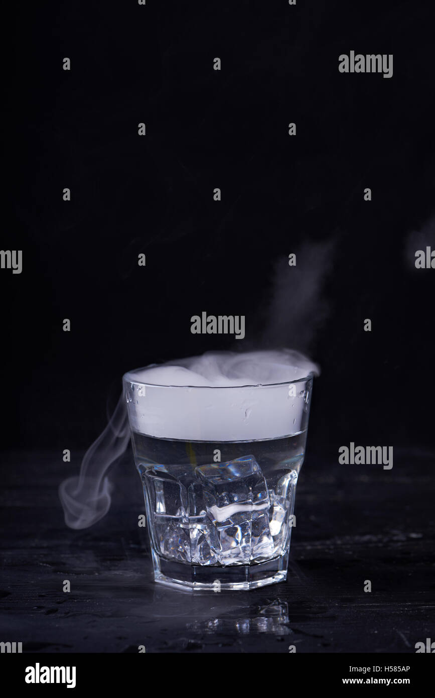 Hot water with a lot of steam in a glass at a black background. Dark photo. Concept photo: three state of water - ice, water, st Stock Photo