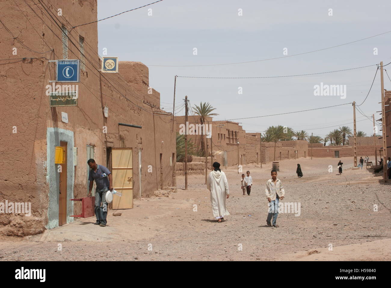 Main street of a small desert town in the Sahara desert, Southern Morocco. Shown mud-brick buildings and man in traditional robe Stock Photo