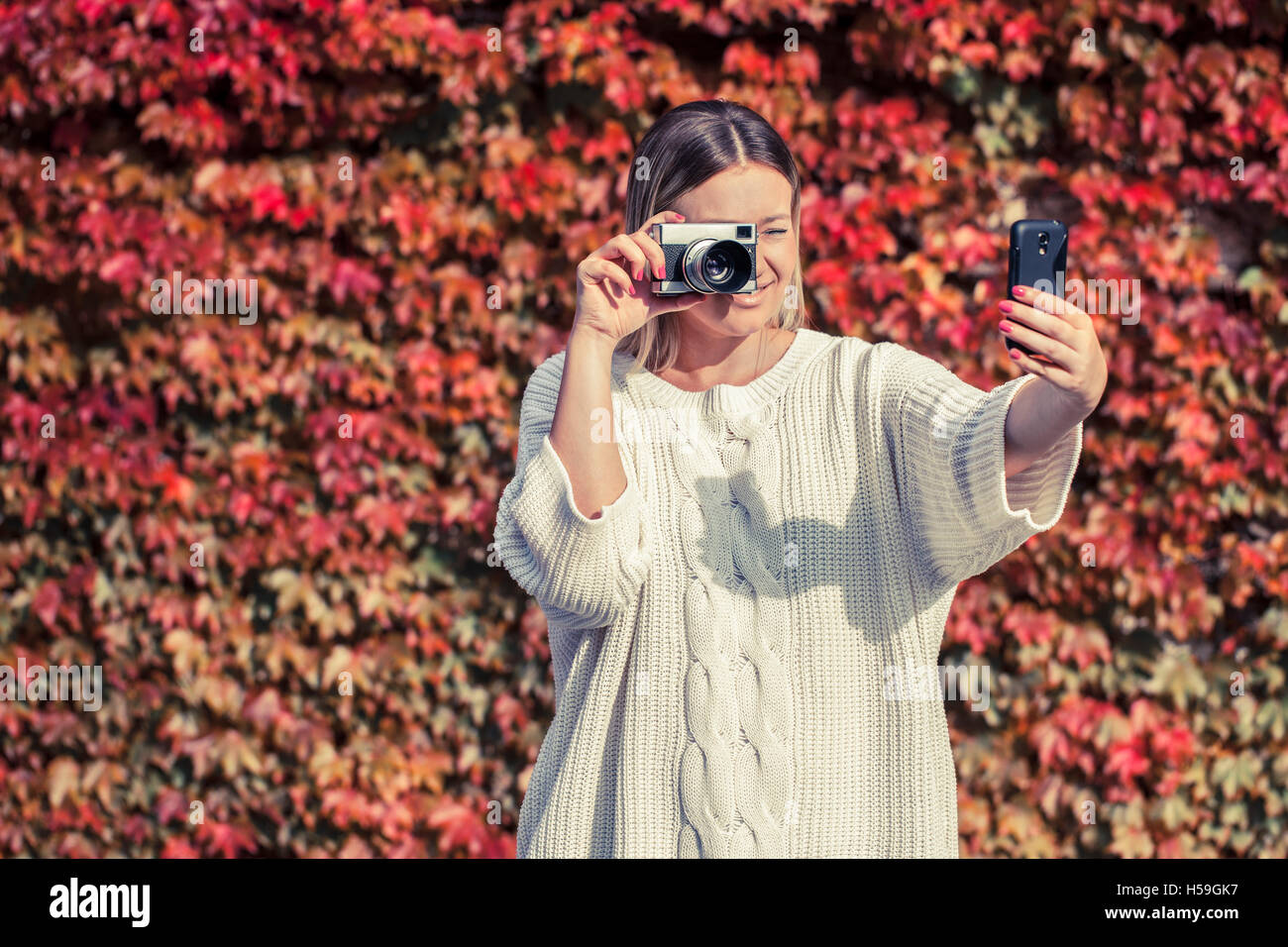 Young woman holding old camera in her hand and making selfie with mobile phone Stock Photo