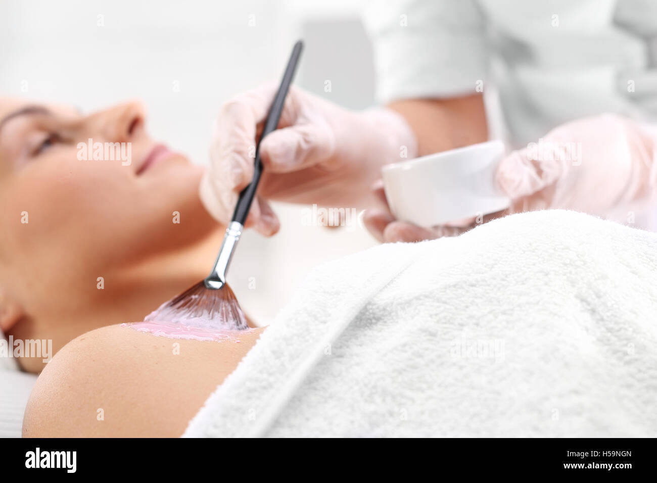 Beautiful neckline, skin care. The woman in the beauty salon, beautician brush mask is applied to the neck Stock Photo