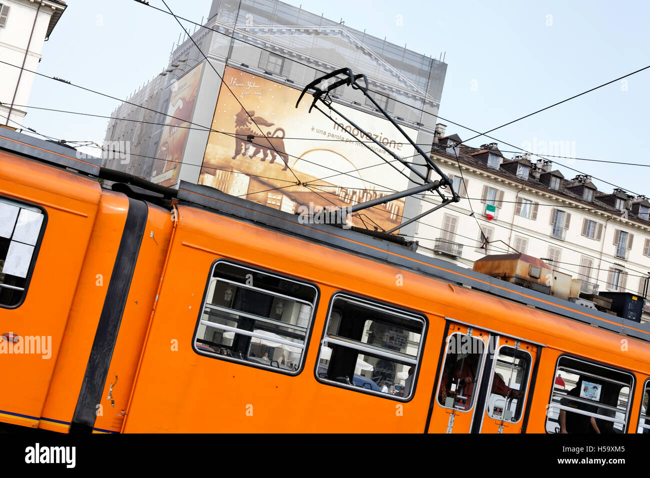 Slanted view of orange coloured tram passing an orange coloured bilboard on the side of an apartment building,Turin,Italy Stock Photo