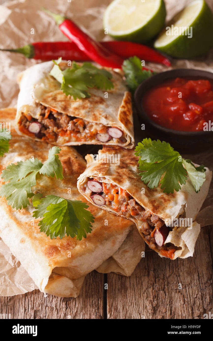 Mexican street food: chimichanga with minced meat close-up on the table. Vertical Stock Photo