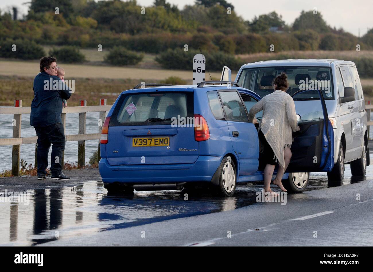 RETRANSMITTING ADDING CAPTION INFORMATION The male driver of the silver van (right) stops to help a lady and a baby from the blue car after it became stranded in the high tide on The Strood crossing between Mersea Island and mainland Essex. Stock Photo