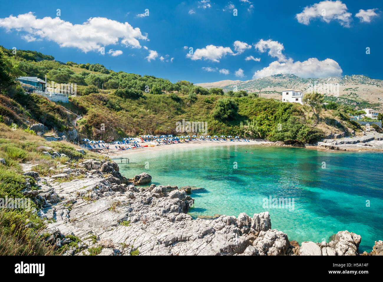 Kassiopi Beach, Corfu Island, Greece. Sunbeds and parasols (sun umbrella) on the beach. Tourists relaxing on the beach. Stock Photo